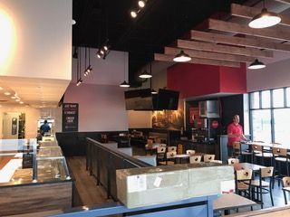 Interior of a restaurant with tables, counter, and a man at the counter.