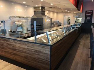 Interior of a restaurant with a food preparation area behind a long counter. Wood paneling and stainless steel accents.