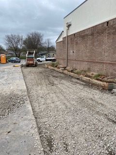 Construction site with a skid steer, gravel path, and brick building.