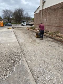 A worker compacts gravel with a machine near a building. Construction site.