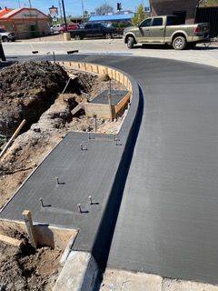 Freshly poured concrete sidewalk with metal studs, curving around a construction site.