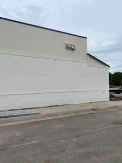 Exterior of a building with white walls. Basketball hoop mounted on upper section. Cloudy sky.