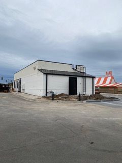 White building with black trim, a ladder, and a partially visible circus tent under a cloudy sky.