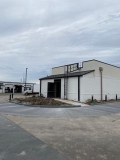 White industrial building with black trim, ramp, and a ladder against the side, under cloudy sky.
