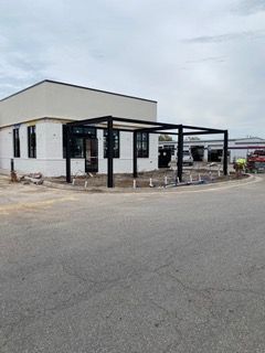 A white building with a black pergola under construction. Gray asphalt in the foreground.