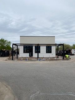 Building under construction; white walls, black frame, gray sky, parking lot in foreground.