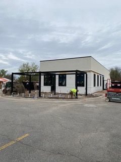 Building construction site; black pergola, white building, worker, concrete, overcast sky.
