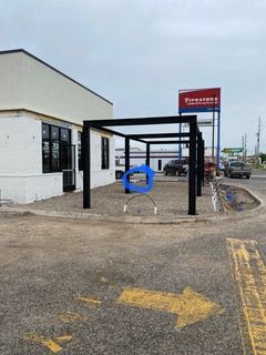 Black metal pergola outside a white building next to a Firestone sign.