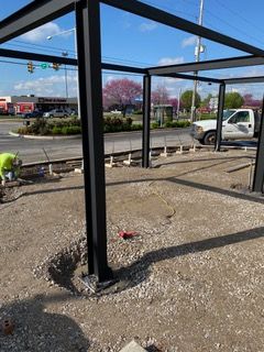 Steel frame construction of a building exterior, set on gravel. Person works nearby.