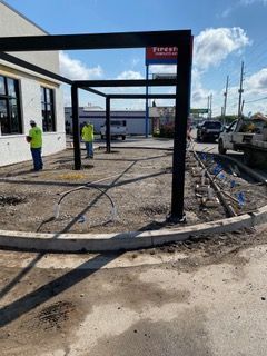 Construction site with workers, black metal canopy, and a Firestone sign in the background.