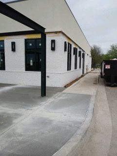 Exterior of a white brick building with black windows and a concrete ramp leading to the entrance.