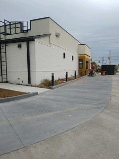 Drive-thru lane at a fast-food restaurant with a concrete surface, building is white and tan. Gray sky.