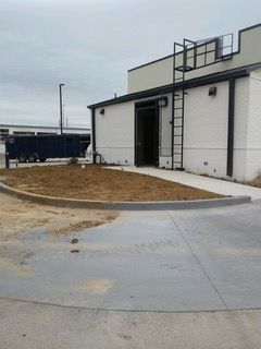 Exterior of a building with a door, ramp, ladder, and a trailer in the background.