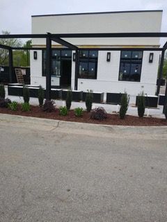 White building with black trim, pergola, and landscaping.