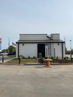 White building with black trim, a ladder, and a spool on a circular driveway.
