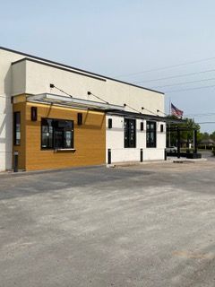 Exterior of a modern building with light and dark color blocks, drive-up window. Paved parking lot in front.