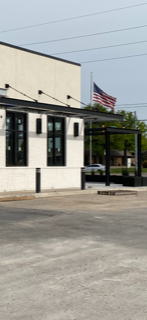 White building with black trim, American flag at half-staff, and parked cars on a gray asphalt lot.