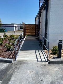 Ramp with metal handrails leading to a building entrance. Blue sky and landscaping visible.