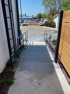 Ramp with handrails leading to an outdoor parking lot from a building. Black ladder on the left, wooden paneling on the right.