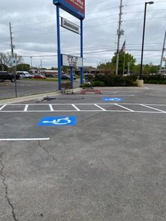 Two blue handicap parking symbols painted on asphalt, under a blue sign that reads 