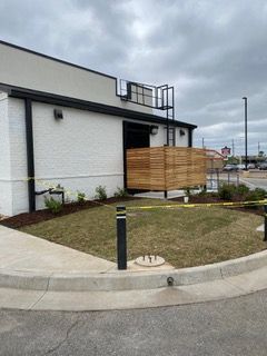 Exterior view of a building with a wooden fence. White brick and black trim, a cloudy sky overhead.