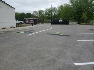 Parking lot with a truck, dumpster, and speed bumps. Gray asphalt with white lines.