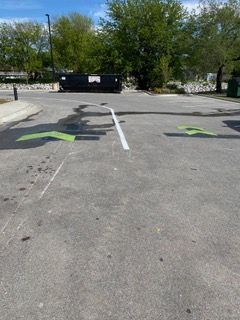 Parking lot with green directional arrows painted on gray asphalt; dumpster in the background.