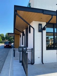 Drive-thru exterior of a white brick building with black trim, metal awning, and a red car.