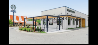 Starbucks store with outdoor seating and orange and white building in the background.