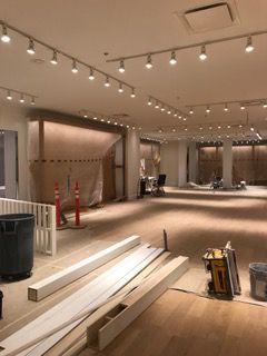Interior of a commercial space under construction; wood flooring, track lighting, construction materials, empty space.