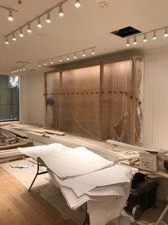Interior during construction, with exposed wooden wall covered in plastic, construction materials on the floor, and track lighting.