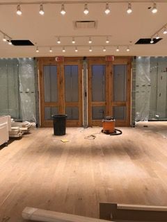 Interior view of a store under construction. Wooden doors, wood flooring, and track lighting are visible.