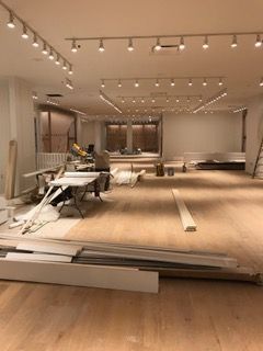Interior of a brightly lit empty store being renovated, with tools and lumber scattered on the floor.