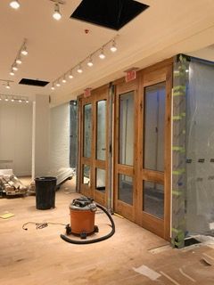 Interior of a building under renovation with wooden doors, a vacuum, and exposed flooring.