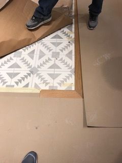 Person standing near patterned flooring covered with paper and wood trim.