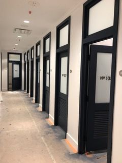 Hallway with multiple black doors, each with frosted glass and a number. White walls, concrete floor.