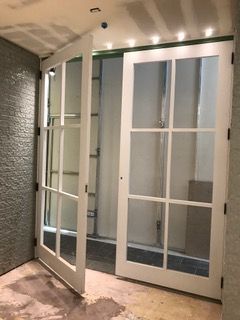 White French doors, one open, in a room with a textured wall and exposed ceiling.