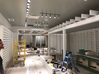 Interior retail space under construction, with track lighting, white walls, and a person observing.