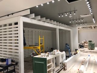 Interior retail space under construction, white latticework walls, green cabinetry, construction tools visible, overhead track lighting.
