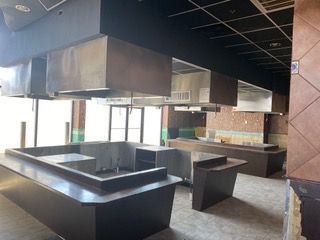 Empty restaurant interior with dark counters, stainless steel hoods, and exposed ceiling.