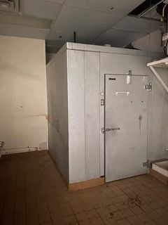 Walk-in cooler in an empty room with a light-colored wall. The door is closed.