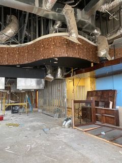 Interior renovation of a commercial space with exposed ductwork, wooden paneling, and construction materials.
