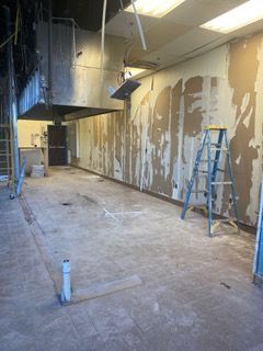 Construction site: interior view of a room with exposed walls, ceiling, and flooring. A ladder stands by the right wall.