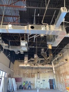 Construction site interior with exposed ceiling ductwork and workers.