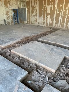 Concrete floor being worked on with sections removed and trenches dug. Interior construction site.