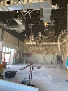 Construction site interior with exposed ductwork, concrete floors, and unfinished walls.