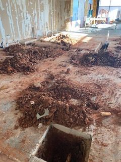 Interior room under construction, dirt and debris on the floor, open square hole.