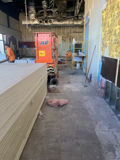 Construction site: interior view. Drywall stacked, orange lift, worker. Walls stripped.