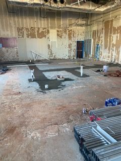 Interior of a room under construction, with exposed walls, cement floor, pipes, and construction materials.
