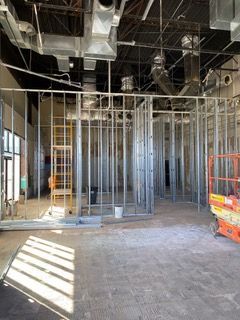 Interior view of a building under construction, showing metal framing for walls, ducts, and unfinished flooring.
